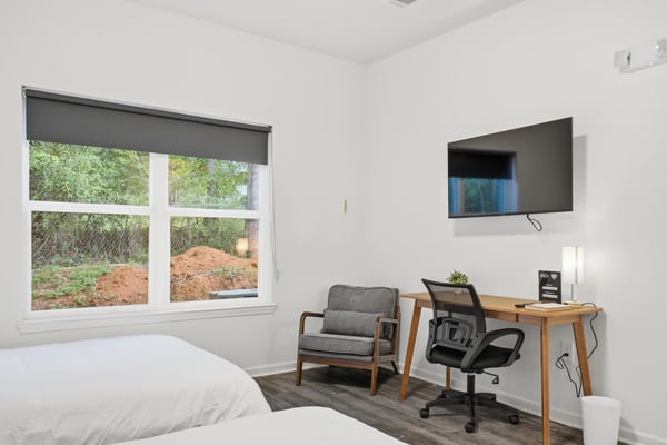 Bright bedroom with two white beds, dark nightstand, abstract wall art, and door to ensuite bathroom