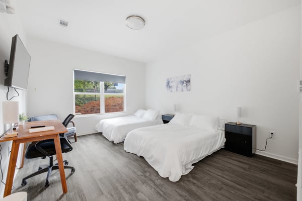 Bright bedroom with two queen beds, work desk, and large window overlooking fields